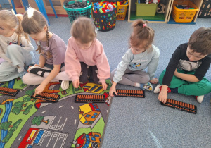 Grupa dzieci siedzi na dywanie i ćwiczy na własnym liczydle