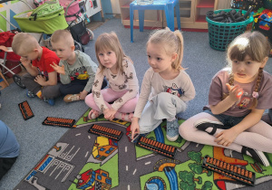 Grupa dzieci siedzi na dywanie i ćwiczy na własnym liczydle