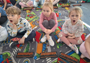 Grupa dzieci siedzi na dywanie i ćwiczy na własnym liczydle