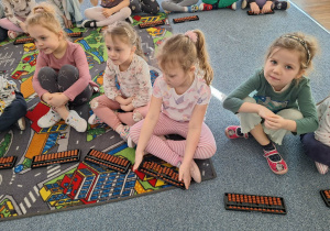 Grupa dzieci siedzi na dywanie i ćwiczy na własnym liczydle