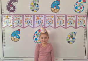 Nadia stoi i pozuje do zdjęcia na tle urodzinowej dekoracji