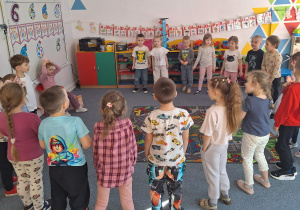 Dzieci stoją na dywanie i śpiewają Nadii sto lat