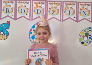 Nadia stoi i pozuje do zdjęcia na tle urodzinowej dekoracji