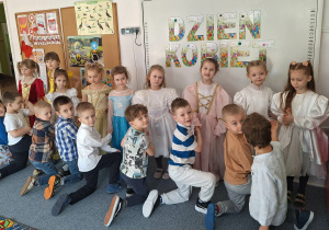 Chłopcy klęczą przed dziewczynkami ubranymi w stroje balowe