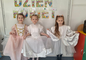 Trzy dziewczynki w strojach balowych pozują do zdjęcia