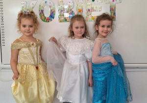 Trzy dziewczynki w strojach balowych pozują do zdjęcia