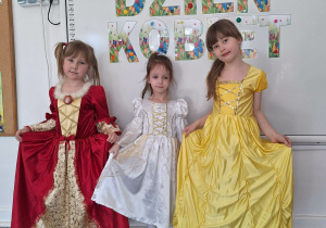 Trzy dziewczynki w strojach balowych pozują do zdjęcia