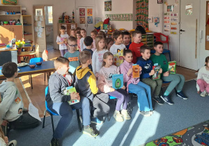 Grupa uczniów siedzi na krzesłach i przygotowuje się do czytania bajek i wierszy przedszkolakom