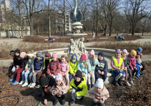 Grupa dzieci stoi przed fontanną w parku