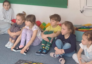 Dzieci siedzą na dywanie i słuchają wierszy