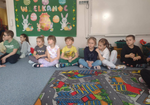 Dzieci siedzą na dywanie i słuchają wierszy