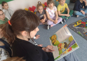 Uczenica siedzi na krześle i czyta wiersz przedszkolakom