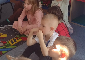Dzieci siedzą na dywanie i słuchają wierszy