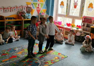 Trójka dzieci stoi na dywanie i recytuje wiersz