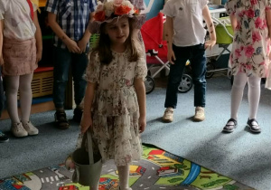 Dziewczynka "Pani wiosna" stoi na dywanie i z grupą dzieci śpiewa piosenkę