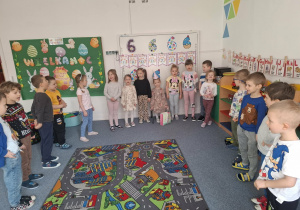 Grupa dzieci stoi na dywanie i śpiewa Laurze 100 lat