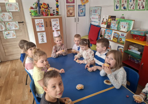 Dzieci siedzą przy stole i jedzą urodzinowe babeczki