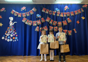 Troje dzieci stoi z dyplomami i torebkami w dłoniach