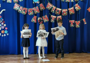 troje dzieci z ilustracjami w dłoniach recytuje wiersz