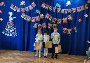 Troje dzieci z dyplomami i torebkami z upominkami