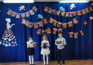 Troje dzieci a ilustracjami recytuje wiersz