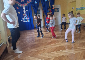 Grupa dzieci na sali gimnastycznej ćwiczy z p.prowadzącym