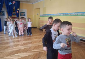 Grupa dzieci na sali gimnastycznej ćwiczy z p.prowadzącym