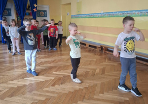 Grupa dzieci na sali gimnastycznej ćwiczy z p.prowadzącym