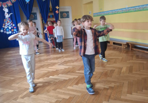 Grupa dzieci na sali gimnastycznej ćwiczy z p.prowadzącym