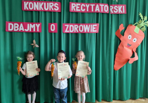 Dzieci stoją na środku sali z dyplomem i nagrodą za udział w konkursie