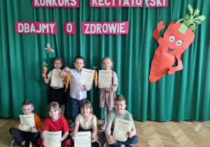 Dzieci z grupy III i IVstoją na środku sali i pozują do zdjęcia z dyplomami za udział w konkursie