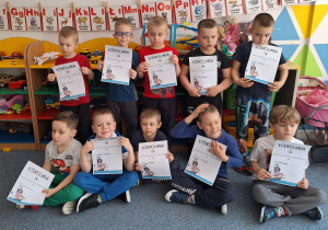 Chłopcy stoją na dywanie i pozują do zdjęcia z dyplomami