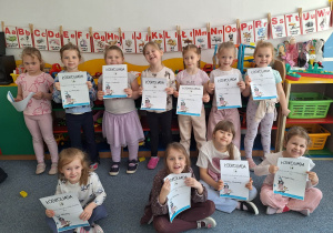 Dziewczynki stoją na dywanie i pozują do zdjęcia z dyplomami