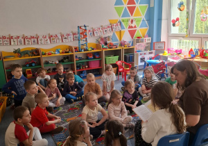 Dzieci siedzą na dywanie i słuchają czytającej mamy i siostry Ani