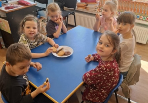 Grupa dzieci siedzi przy stoliku i degustuje smakołyki od Krzysia