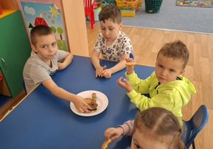 Grupa dzieci siedzi przy stoliku i degustuje smakołyki od Krzysia