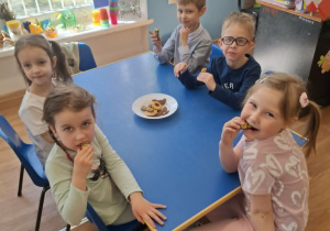 Grupa dzieci siedzi przy stoliku i degustuje smakołyki od Krzysia