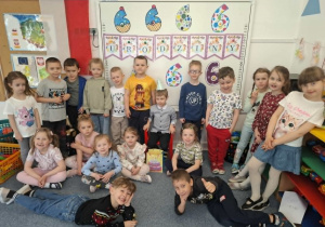 Krzysiu siedzi na krzesełku i pozuje do zdjęcia z całą grupą dzieci