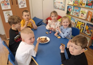 Grupa dzieci siedzi przy stoliku i degustuje smakołyki od Krzysia