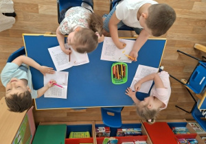 Grupa dzieci siedzi przy stolikach i koloruje obrazki w książeczce