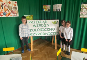 Troje dzieci przed tablicą z napisem przegląd wiedzy ekologiczno-przyrodniczej