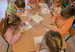 Dzieci siedzą przy stole i ozdabiają ceramiczne kwiaty