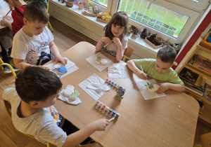 Dzieci siedzą przy stole i ozdabiają ceramiczne kwiaty
