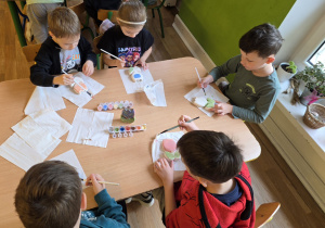 Dzieci siedzą przy stole i ozdabiają ceramiczne kwiaty