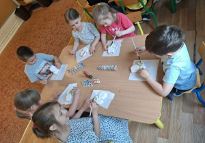 Grupa dzieci siedzi przy stole i maluje farbami ceramiczny kwiatek