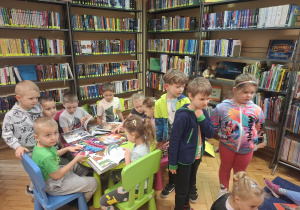 Grupa dzieci ogląda w bibliotece książeczki w kąciku czytelniczym