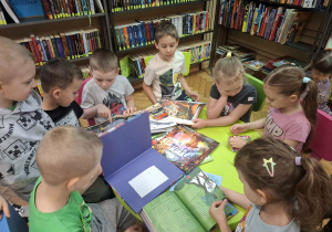 Grupa dzieci ogląda w bibliotece książeczki w kąciku czytelniczym