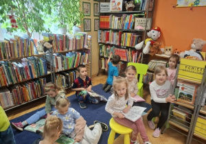 Grupa dzieci ogląda w bibliotece książeczki w kąciku czytelniczym