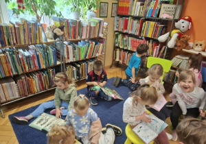 Grupa dzieci ogląda w bibliotece książeczki w kąciku czytelniczym