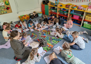 Dzieci leżą na dywanie i słuchają p.prowadzącej, która czyta im książkę